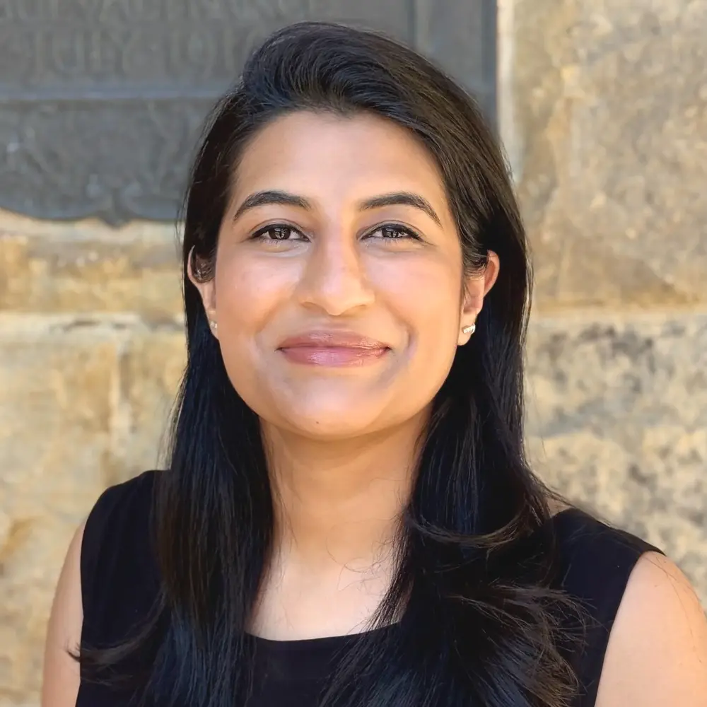 Headshot of Natalya Adam-Rahman, smiling, in front of a stone wall